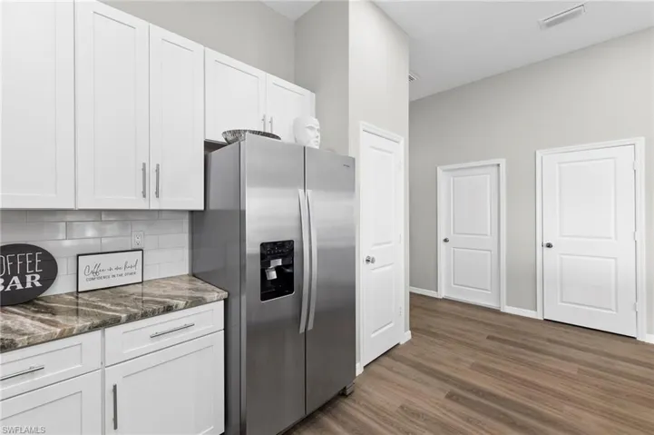 Kitchen featuring stainless steel fridge, white cabinetry, dark stone counters, and dark wood-style floors