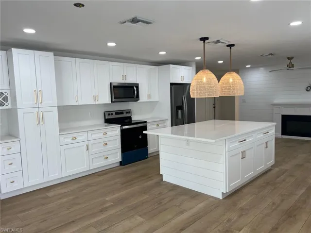 Kitchen with stainless steel appliances, white cabinets, a fireplace, and a center island