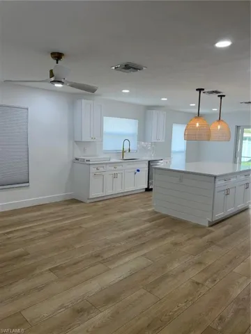 Kitchen with white cabinets, a kitchen island, a ceiling fan, and light wood-style floors