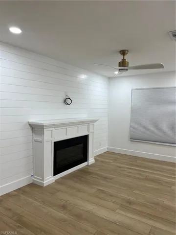 Detailed view of a glass covered fireplace, wood finished floors, and a ceiling fan
