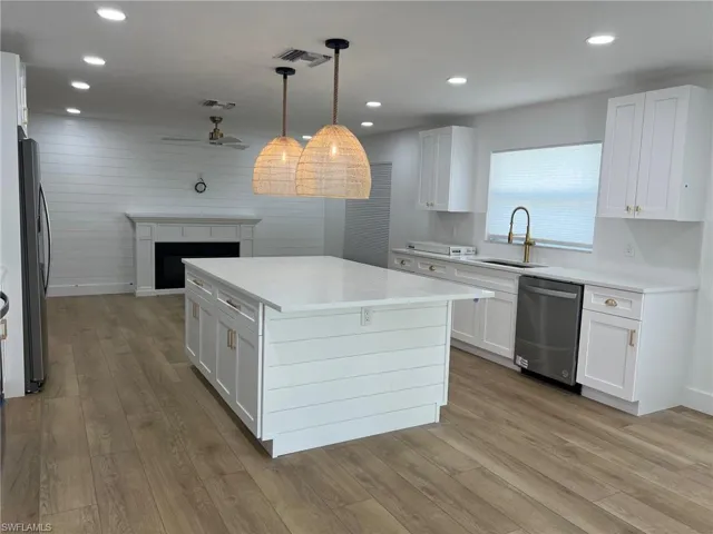 Kitchen featuring white cabinets, a fireplace, light wood-style flooring, stainless steel appliances, and wood walls