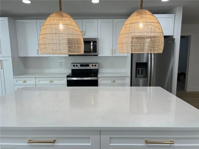 Kitchen featuring white cabinetry, stainless steel appliances, backsplash, light stone countertops, and recessed lighting