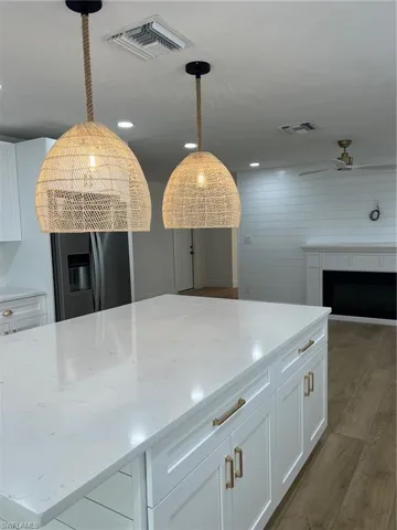 Kitchen featuring refrigerator, light wood finished floors, white cabinetry, a fireplace, and light stone counters