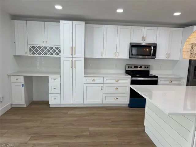 Kitchen with stainless steel appliances, white cabinets, dark wood-type flooring, light stone countertops, and recessed lighting