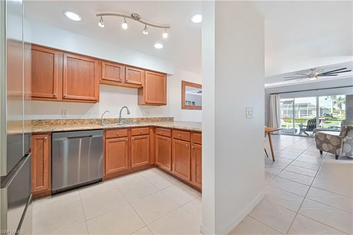 Kitchen with sink, ceiling fan, light tile patterned floors, light stone counters, and stainless steel appliances