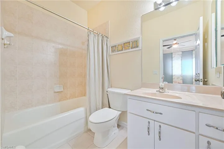 Full bathroom featuring ceiling fan, tile patterned flooring, toilet, shower / tub combo with curtain, and vanity