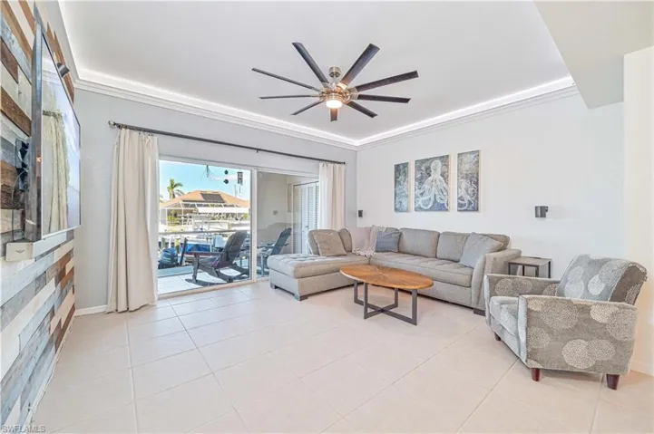 Living room with ceiling fan, ornamental molding, and light tile patterned flooring