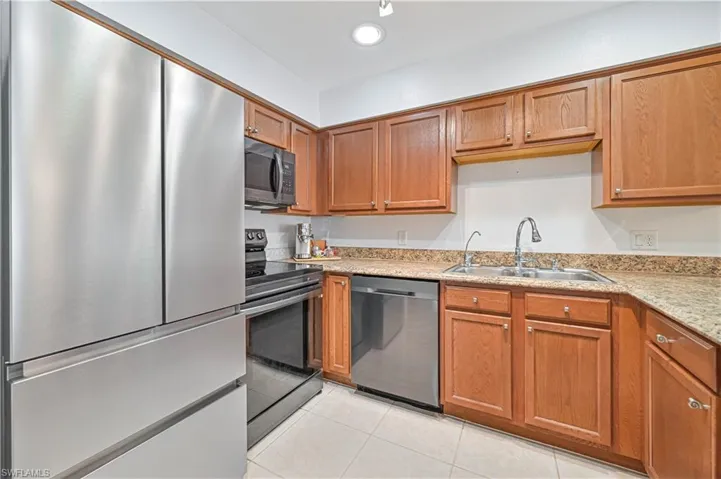 Kitchen with light tile patterned flooring, appliances with stainless steel finishes, light stone countertops, and sink