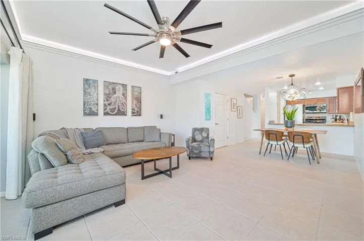 Living room with ceiling fan with notable chandelier and light tile patterned flooring