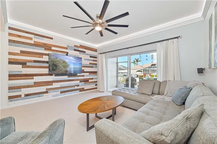 Tiled living room featuring ceiling fan, wood walls, and ornamental molding