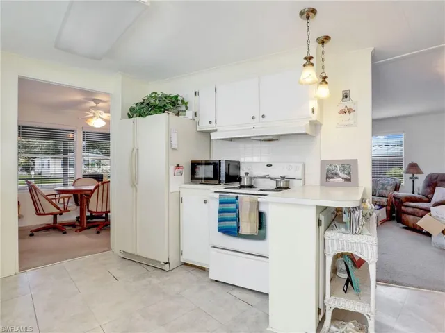 Kitchen with decorative light fixtures, white appliances, tasteful backsplash, and light colored carpet