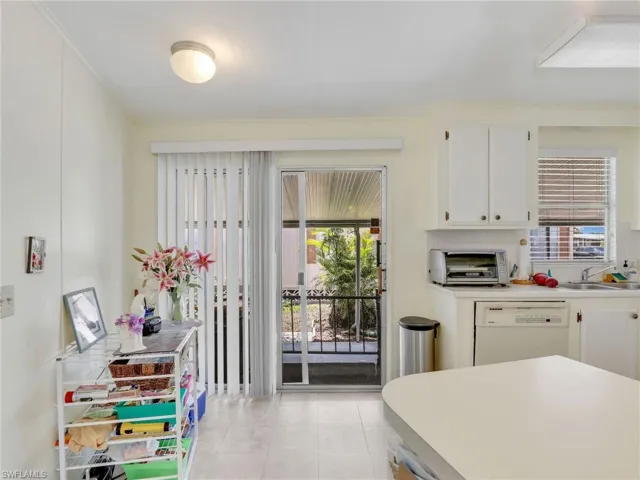 Kitchen featuring dishwasher, sink, white cabinetry, and light tile flooring