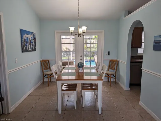 Indoor dining room for 6, featuring a chandelier, dark tile patterned flooring, french doors, and arched walkways
