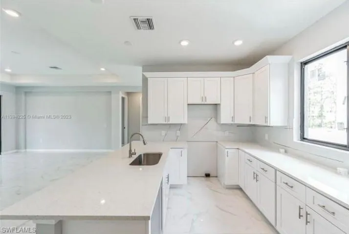 Kitchen featuring white cabinets, sink, backsplash, and light tile floors