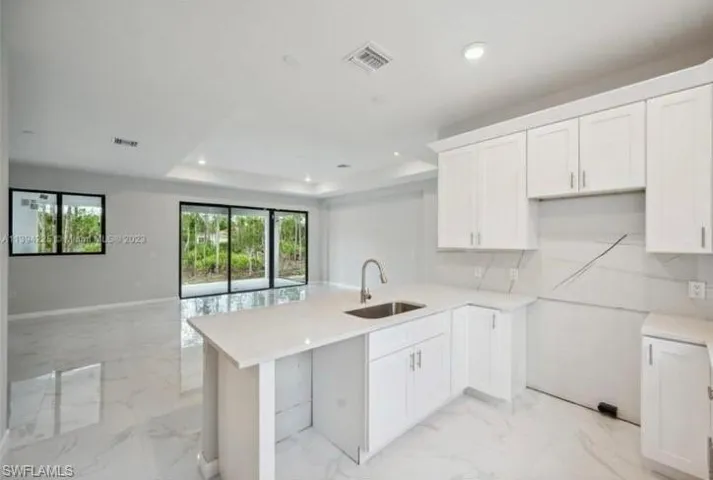 Kitchen with light stone counters, sink, white cabinets, and light tile floors