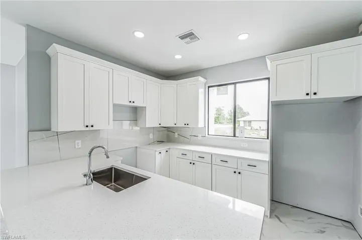 Kitchen with white cabinets, light stone counters, backsplash, sink, and light tile floors