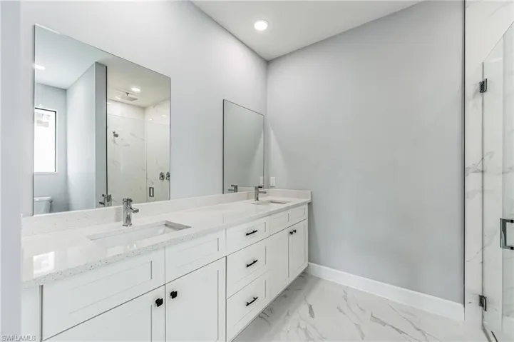 Bathroom with dual sinks, vanity with extensive cabinet space, walk in shower, tile floors, and toilet