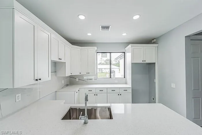 Kitchen with white cabinets, sink, tasteful backsplash, and light stone countertops