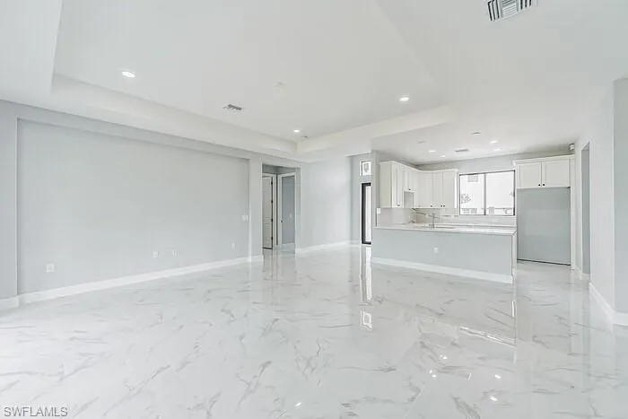 Unfurnished living room featuring sink, a tray ceiling, and light tile floors