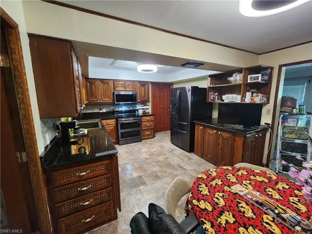 Kitchen with appliances with stainless steel finishes, dark stone counters, tasteful backsplash, stone finish floors, and open shelves