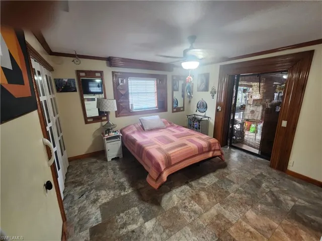 Primary Bedroom with access to outside, multiple windows, stone finish flooring, ornamental molding, and a ceiling fan