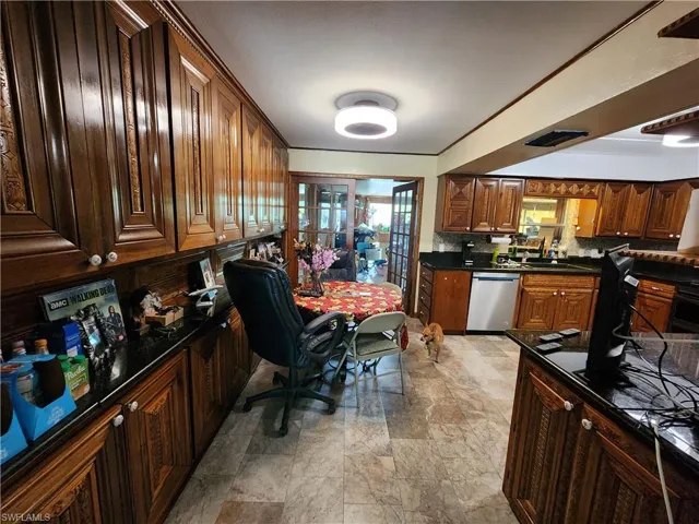 Kitchen featuring dishwasher, light stone finish flooring, decorative backsplash, built in desk, and dark stone counters