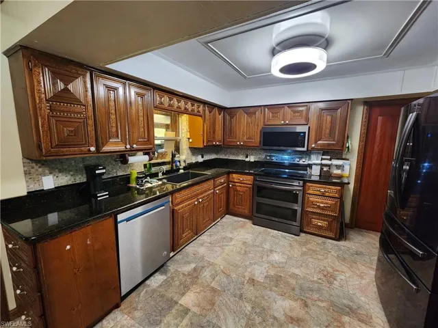 Kitchen with backsplash, appliances with stainless steel finishes, dark stone counters, and stone finish flooring