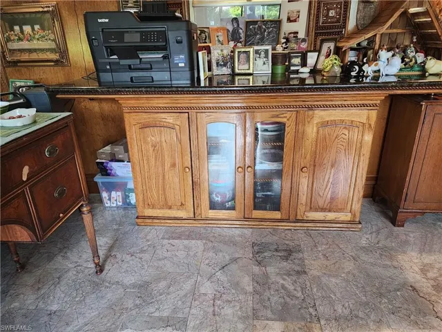 Bar with glass insert cabinets, wooden walls, and dark stone countertops
