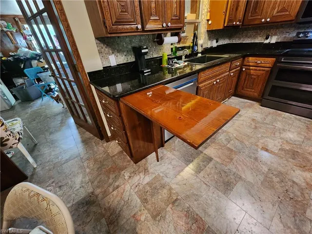 Kitchen featuring decorative backsplash, range with two ovens, light stone finish flooring, and brown cabinetry