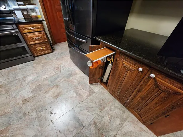 Kitchen featuring stove, dark stone countertops, freestanding refrigerator, and light stone finish flooring