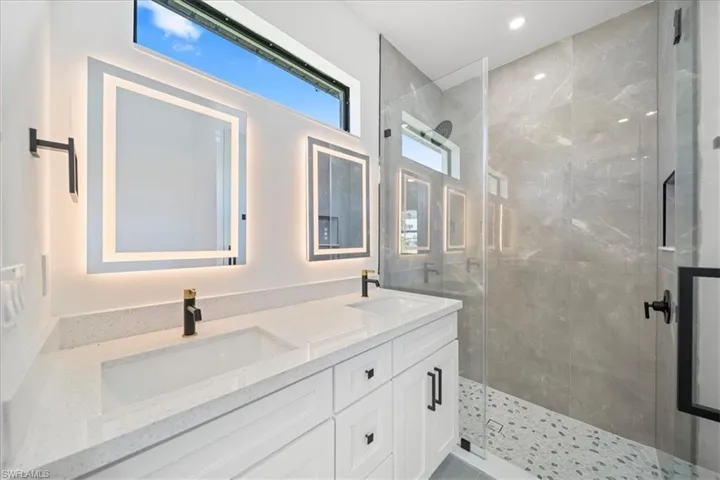 Spa-inspired bathroom featuring a dual-sink quartz vanity, illuminated designer mirrors
