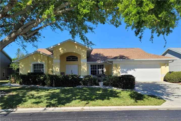 View of front of property featuring a garage, double entry doors, majestic oak tree  and mature landscaping.