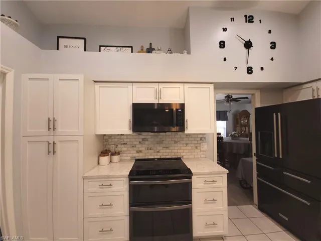 Kitchen featuring white cabinets, appliances with stainless steel finishes, light quartz countertops, tiled back-splash and pantry with pull-outs
