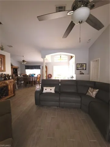 Living room featuring vaulted ceiling, light wood-style tile flooring, a wealth of natural light, and ceiling fan
