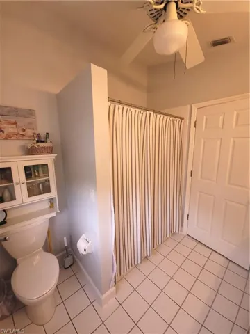 Bathroom featuring tile flooring, ceiling fan, curtained shower, and toilet