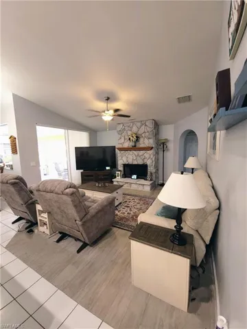 Living room with ceiling fan, a stone fireplace, and light wood-type tile flooring