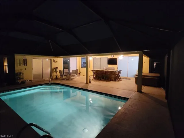 View of pool at night with a patio area
