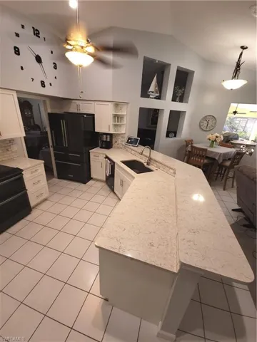 Kitchen featuring refrigerator, sink, kitchen peninsula, ceiling fan, quartz countertops, custom cabinets and recessed lighting