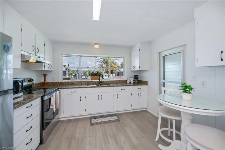 Kitchen with stainless steel appliances, light wood-type flooring, white cabinets, under cabinet range hood, and dark stone counters