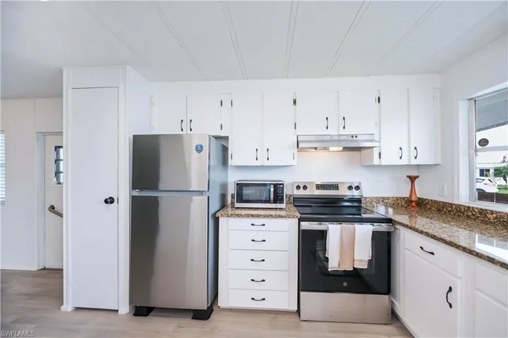 Kitchen with stainless steel appliances, white cabinets, dark stone counters, under cabinet range hood, and light wood-style flooring