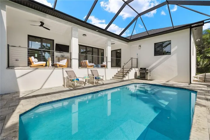 View of pool featuring glass enclosure, a patio area, and ceiling fan