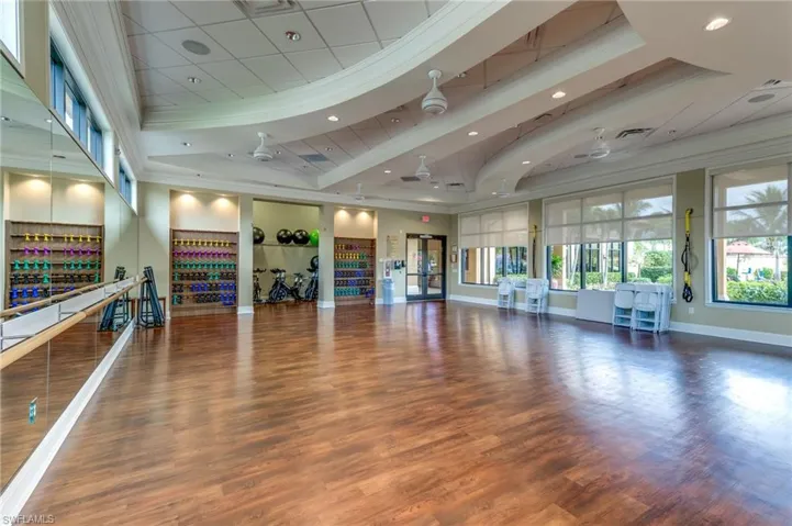 Spacious multi-purpose room featuring wood-finish flooring, mirrored wall with ballet barre, recessed lighting, and large windows with roller shades