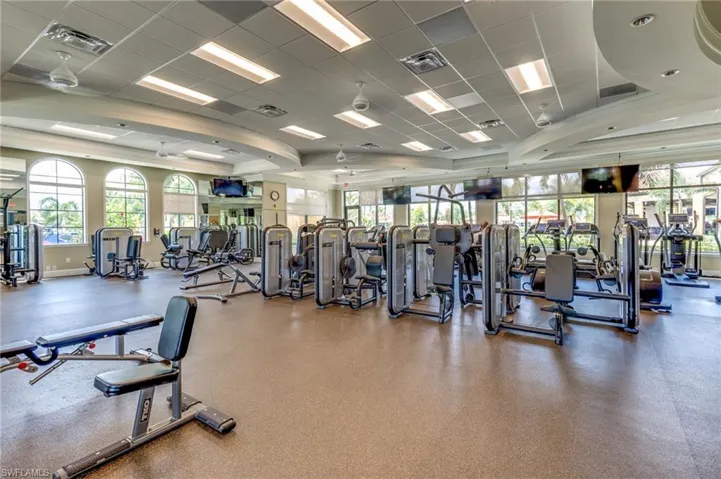 Spacious fitness center featuring a comprehensive array of exercise equipment, high ceilings with recessed lighting, multiple large arched windows, expansive mirror walls, and durable commercial-grade flooring