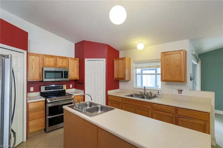 Kitchen featuring vaulted ceiling, stainless steel appliances, light countertops, light tile patterned flooring, and a center island with sink