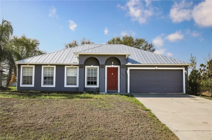 Single story home with an attached garage, a metal roof, driveway, and stucco siding