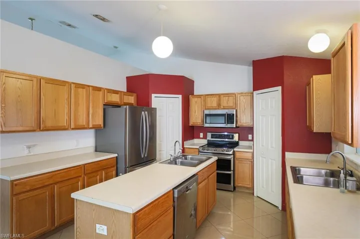 Kitchen with stainless steel appliances, an island with sink, light countertops, pendant lighting, and light tile patterned flooring