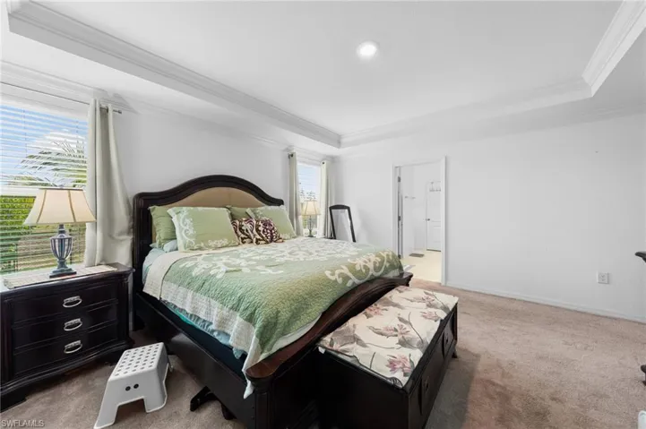 Bedroom featuring a raised ceiling, ornamental molding, light carpet, and baseboards