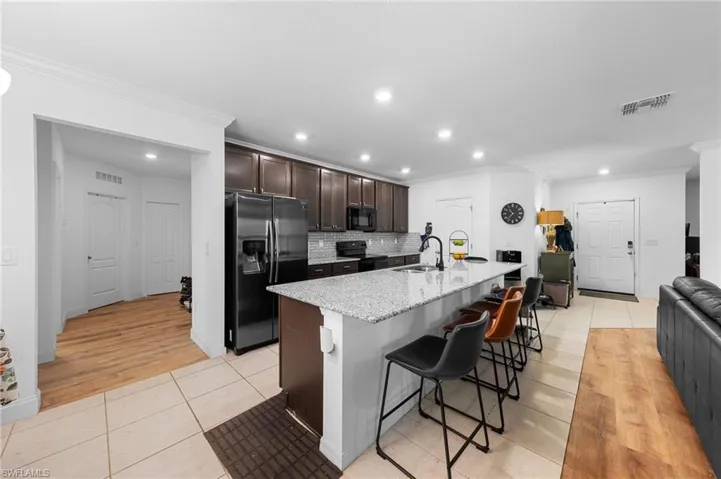 Kitchen featuring black appliances, crown molding, a sink, dark brown cabinets, and light tile patterned floors