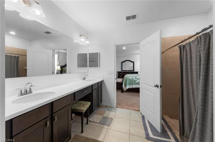 Ensuite bathroom featuring double vanity, tiled shower, tile patterned flooring, recessed lighting, and baseboards