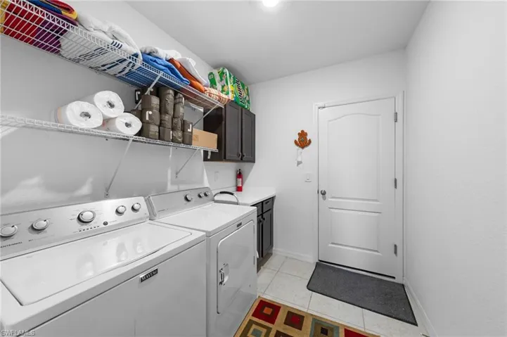 Laundry area featuring cabinet space, washer and dryer, light tile patterned floors, and baseboards